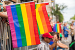 Pride flags being held over a crowd barrier at a Pride Parade